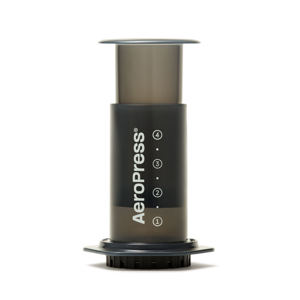The AeroPress Coffee Maker, shown upright on a white background with visible measurement markings and its distinct logo, is ready to brew a smooth, low-acidity cup of coffee using a compostable paper filter.