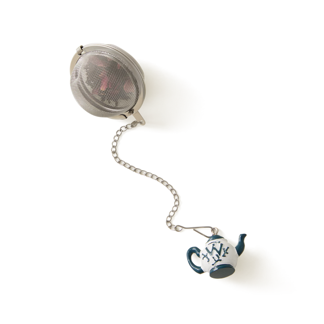 A metal tea infuser ball attached to a chain with a small decorative ceramic teapot charm at the end, set against a white background.