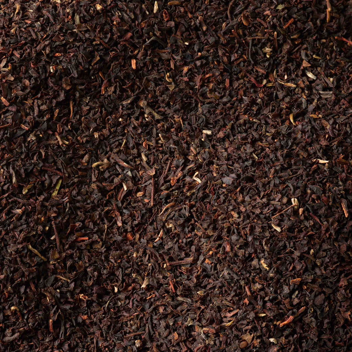 A close-up view of loose leaf English Breakfast Tea, revealing a dense, textured surface with varying sizes and rich shades of dark brown—distinctive qualities of this classic blend.