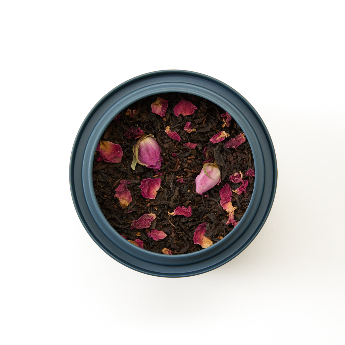 An overhead view of English Rose Loose Leaf Tea—loose black tea blended with dried pink English rose petals—in a round blue tin container, set against a white background.