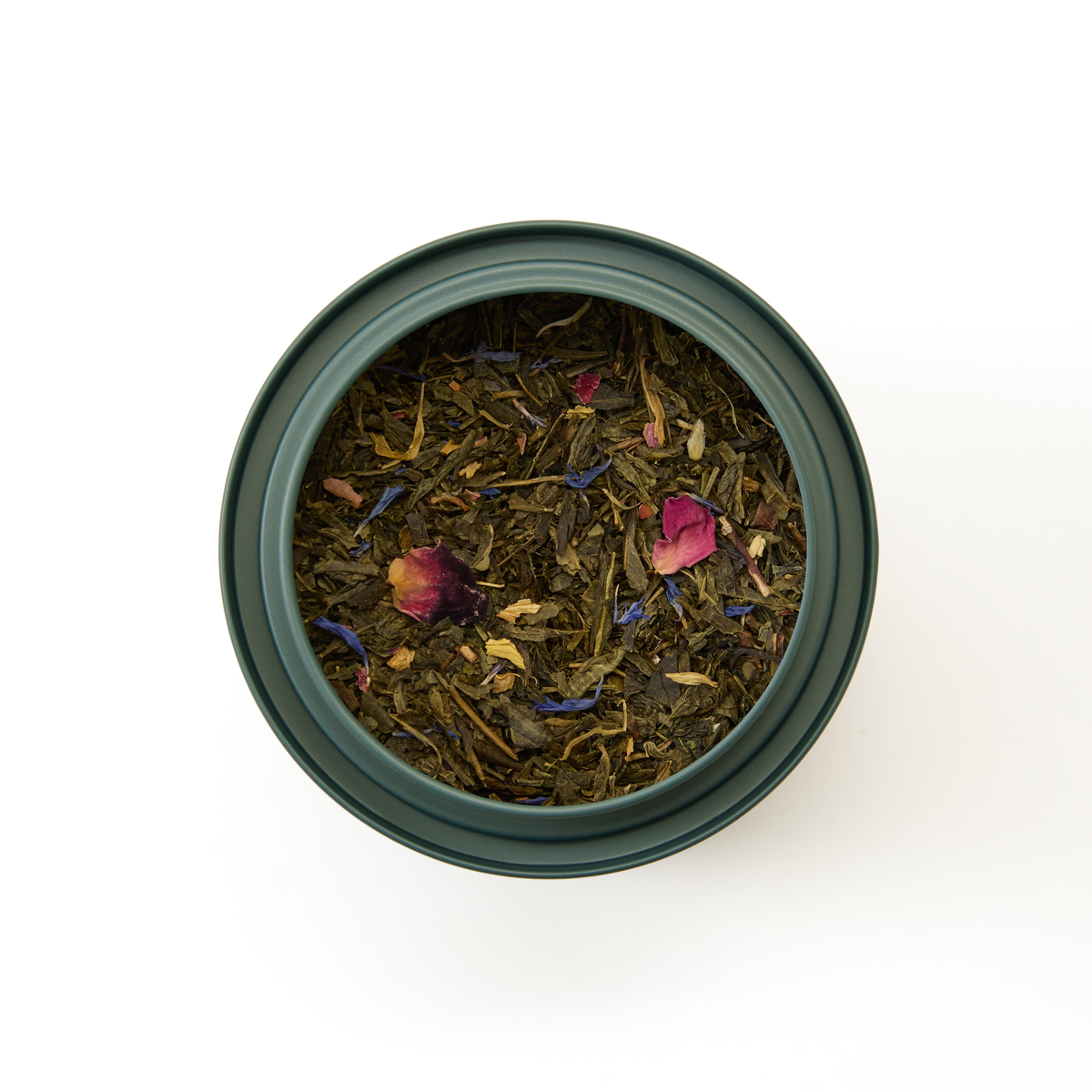 A top-down view of a green container filled with Mango & Bergamot Loose Leaf Tea, featuring fresh green tea leaves and scattered colorful flower petals, set against a white background.