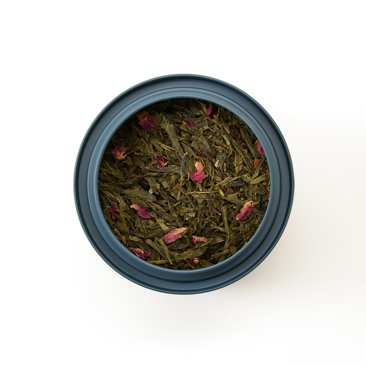 A round black container filled with Cherry Blossom Loose Leaf Tea—sencha green tea blended with small pink flower petals—evokes the delicate beauty of Japanese spring, as seen from above on a white background.