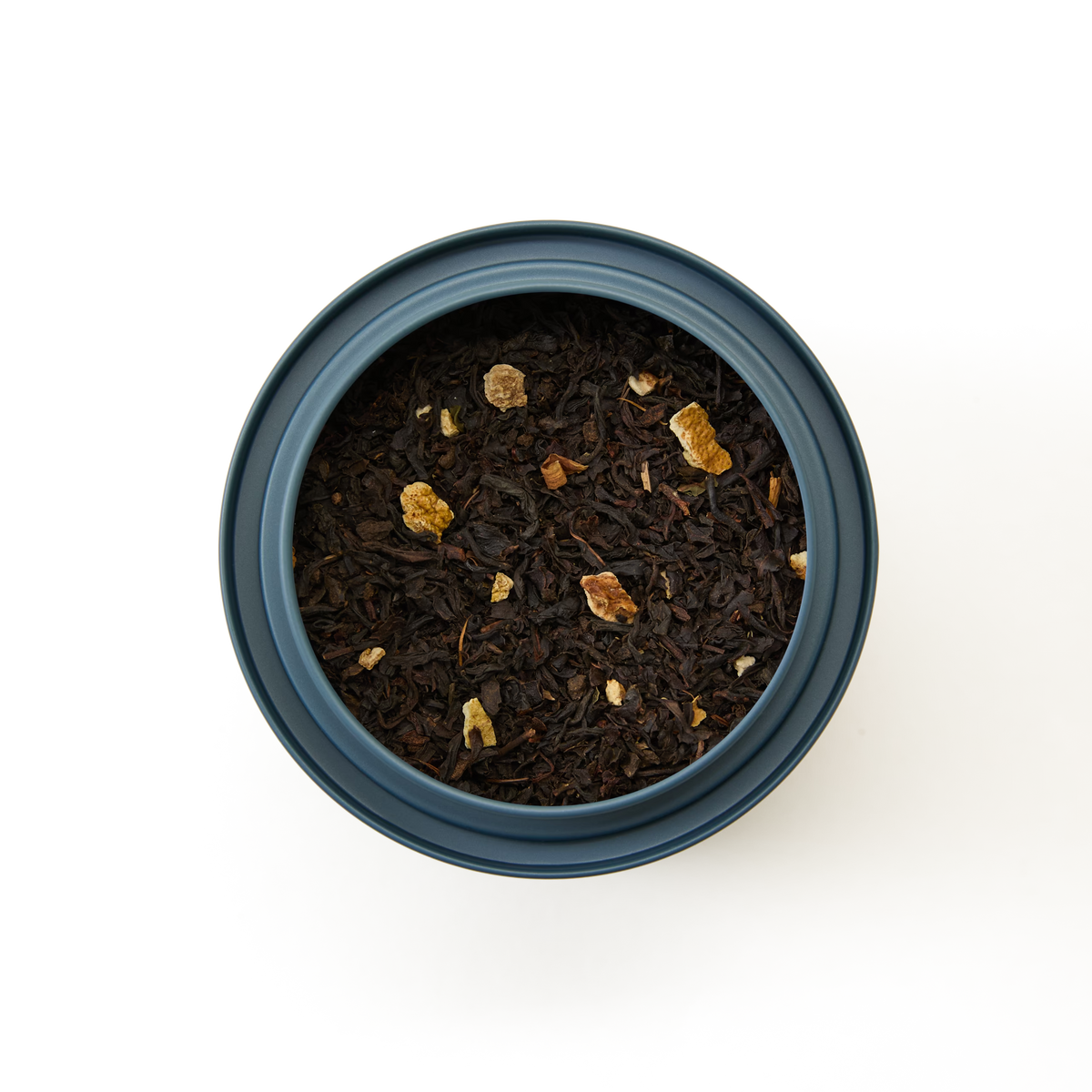 A top-down view of a round, blue container filled with Orange Blossom Loose Leaf Tea—black tea leaves blended with small pieces of dried fruit and citrus peel—perfect for crafting your own floral black tea blend, set against a plain white background.