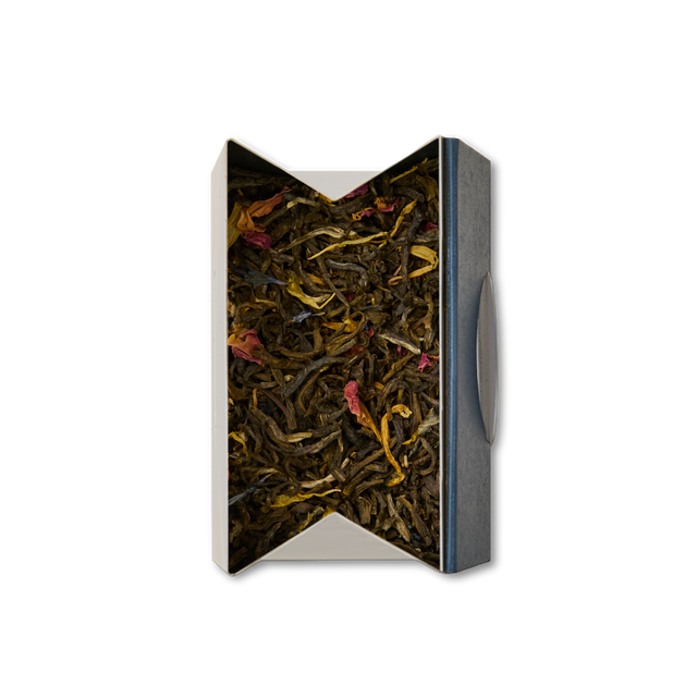 A top-down view of an open, rectangular box filled with Extravagant Earl Grey Loose Leaf Tea—an enticing blend of green and brown leaves interspersed with small pieces of red and yellow petals, offering a delightful assortment that hints at aromatic white earl grey tea with notes of vanilla bergamot.