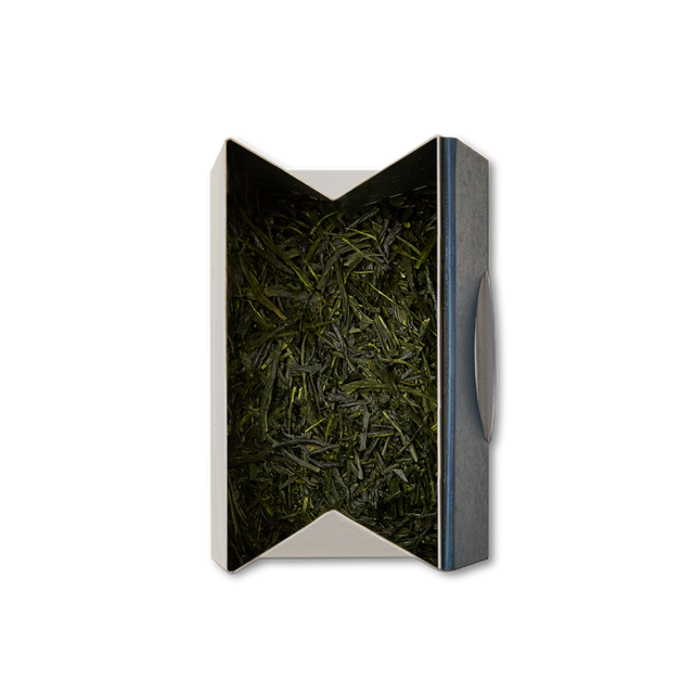 A box with a metallic edge contains Gyokuro Loose Leaf Tea—loose, dark green leaves known for their rich umami flavor—neatly packed inside and viewed from above against a white background.