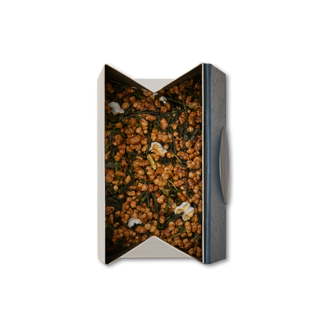 A box of Genmaicha Loose Leaf Tea, featuring visible roasted brown rice and green tea leaves with a few popped rice pieces on top, photographed from above against a white background.