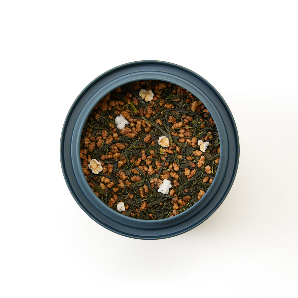 A round tin of Genmaicha Loose Leaf Tea, a classic Japanese green tea blend, showcases vibrant green tea leaves mixed with roasted brown rice and a few popped rice pieces, viewed from above on a white background.