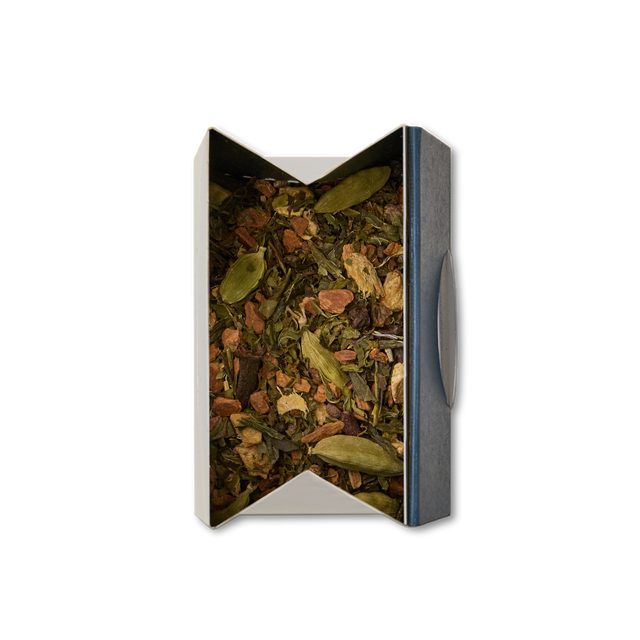 An open rectangular box of Shanghai Chai Loose Leaf Tea filled with cardamom pods and assorted dried spices, viewed from above on a white background.