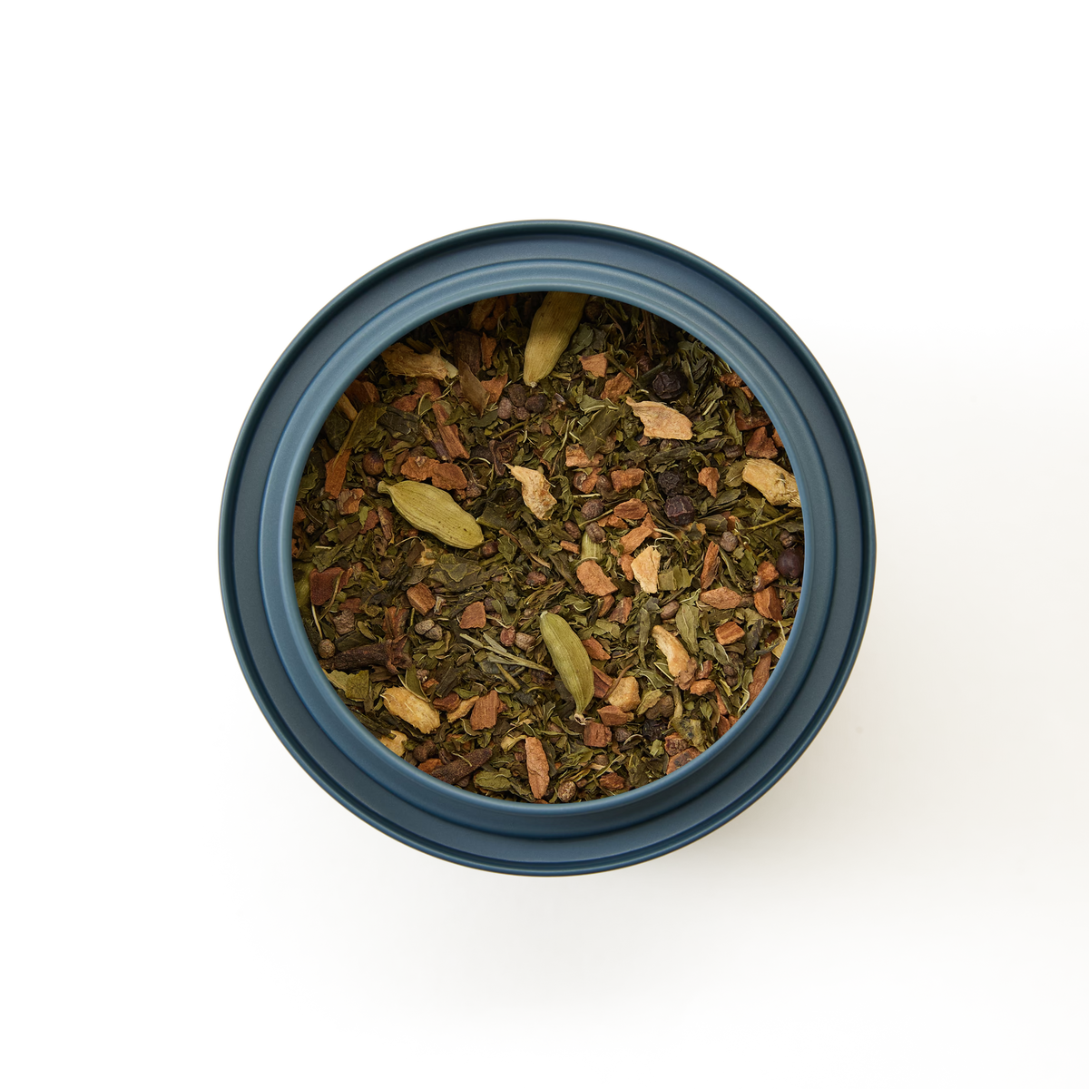 A top-down view of a blue container filled with Shanghai Chai Loose Leaf Tea, showcasing visible herbs, spices, and dried plant pieces against a white background.