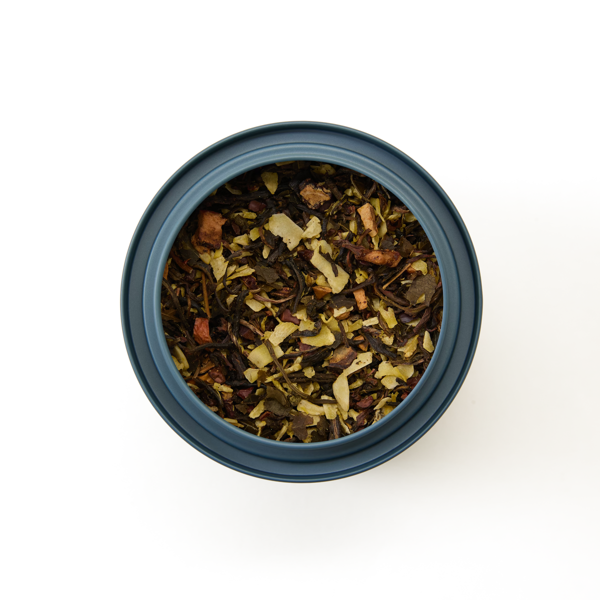A round, blue container of Coconut Truffle Loose Leaf Tea—featuring green leaves, dried fruit pieces, and light-colored flakes like white tea and coconut tea—is viewed from above on a white background.