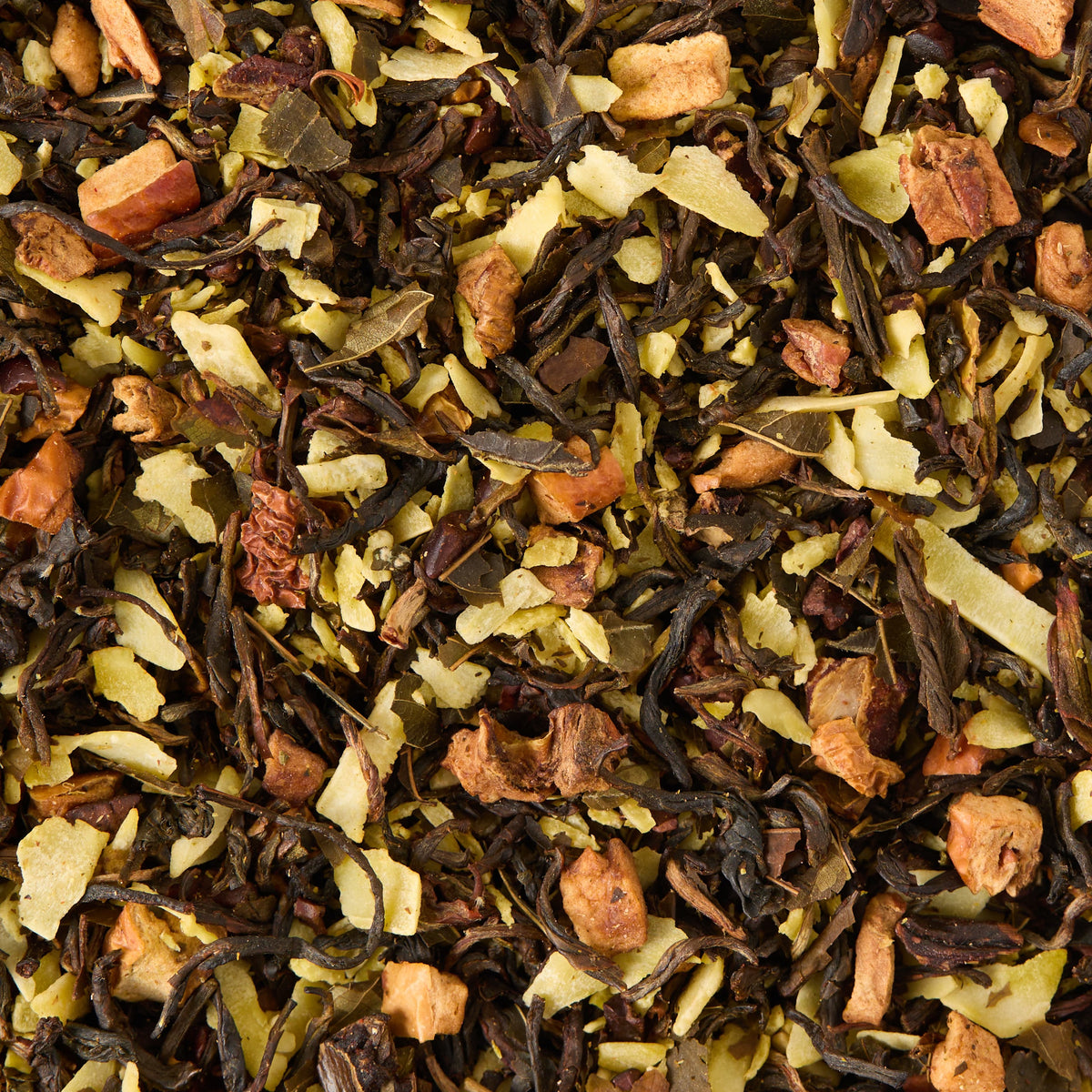 A close-up of Coconut Truffle Loose Leaf Tea, a blend that features dried fruit pieces, shredded coconut, and assorted herbs and leaves, displaying a mix of brown, green, and light tan colors.