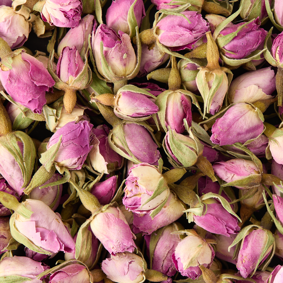 A close-up of Rosebuds Loose Infusion reveals numerous dried pink rosebuds with their delicate petals and green sepals, densely packed together.