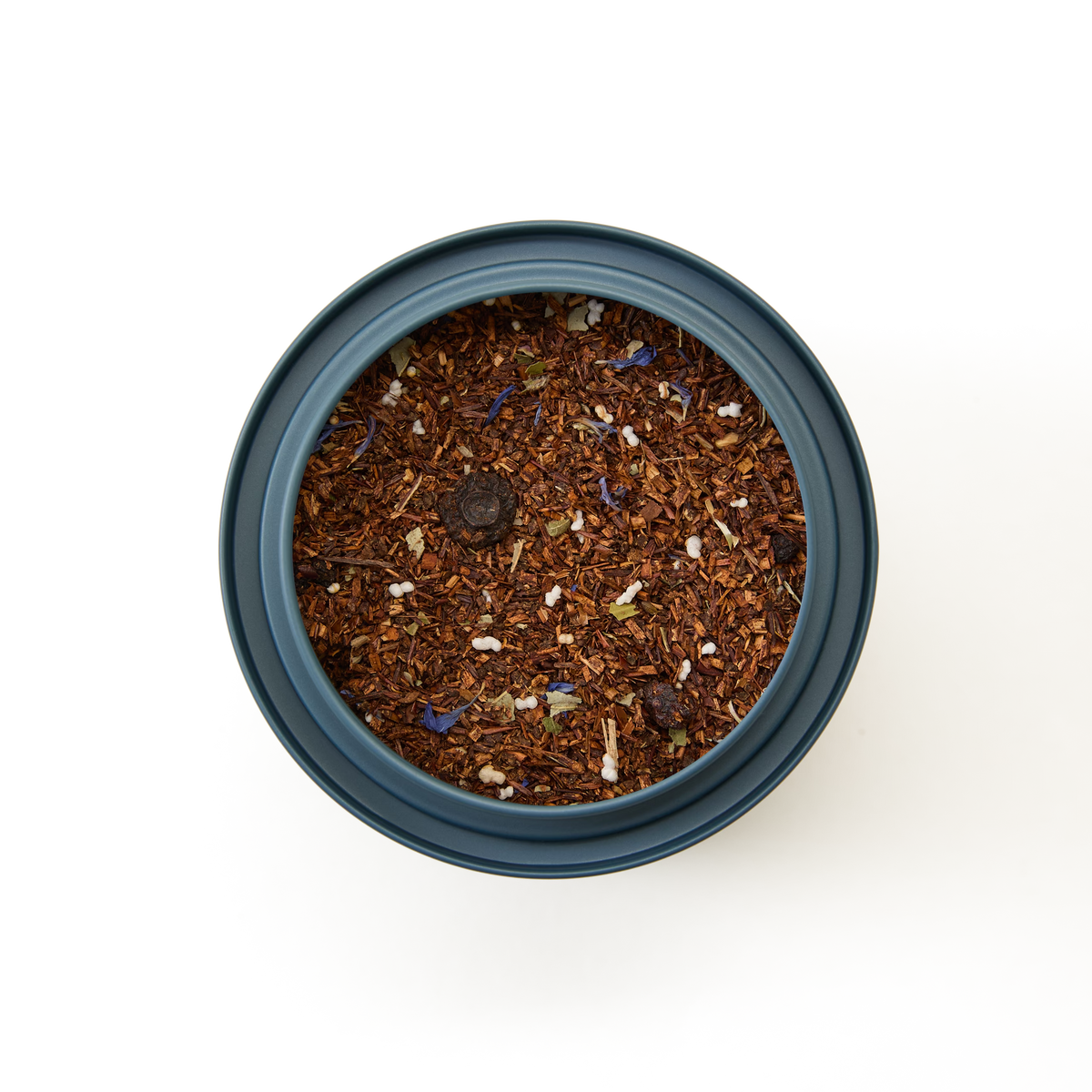 A round container filled with Blueberry Rooibos Loose Leaf Tea, featuring reddish-brown rooibos leaves, scattered blue and white flower petals, and small white granules—this vibrant berry-infused blend is naturally caffeine free. Photographed from above on a plain white background.