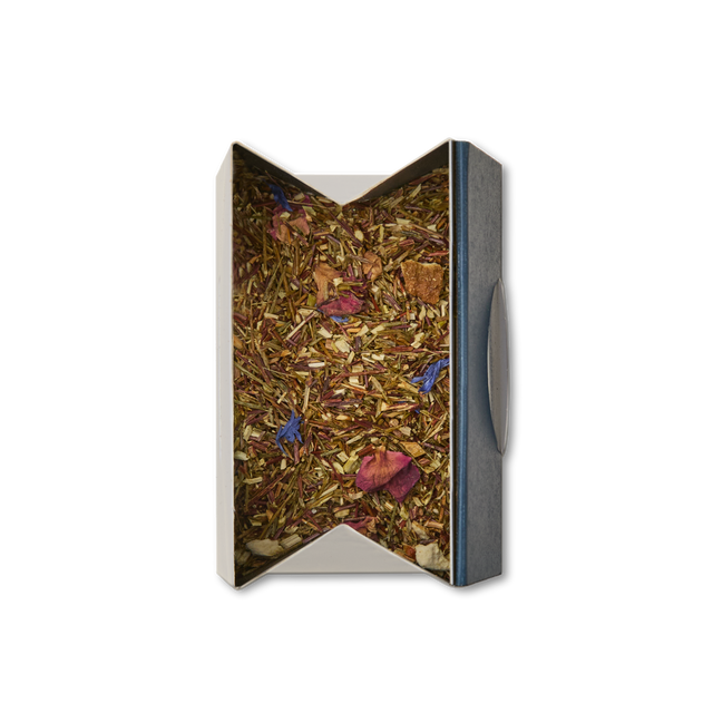 An open box of Rainforest Rooibos Loose Leaf Tea displays reddish-brown leaves and vibrant flower petals nestled inside, viewed from above on a white background. This visually striking herbal blend showcases tropical rooibos—a naturally caffeine-free tea—celebrated for its refreshing flavors and the aromatic allure of exotic botanicals.