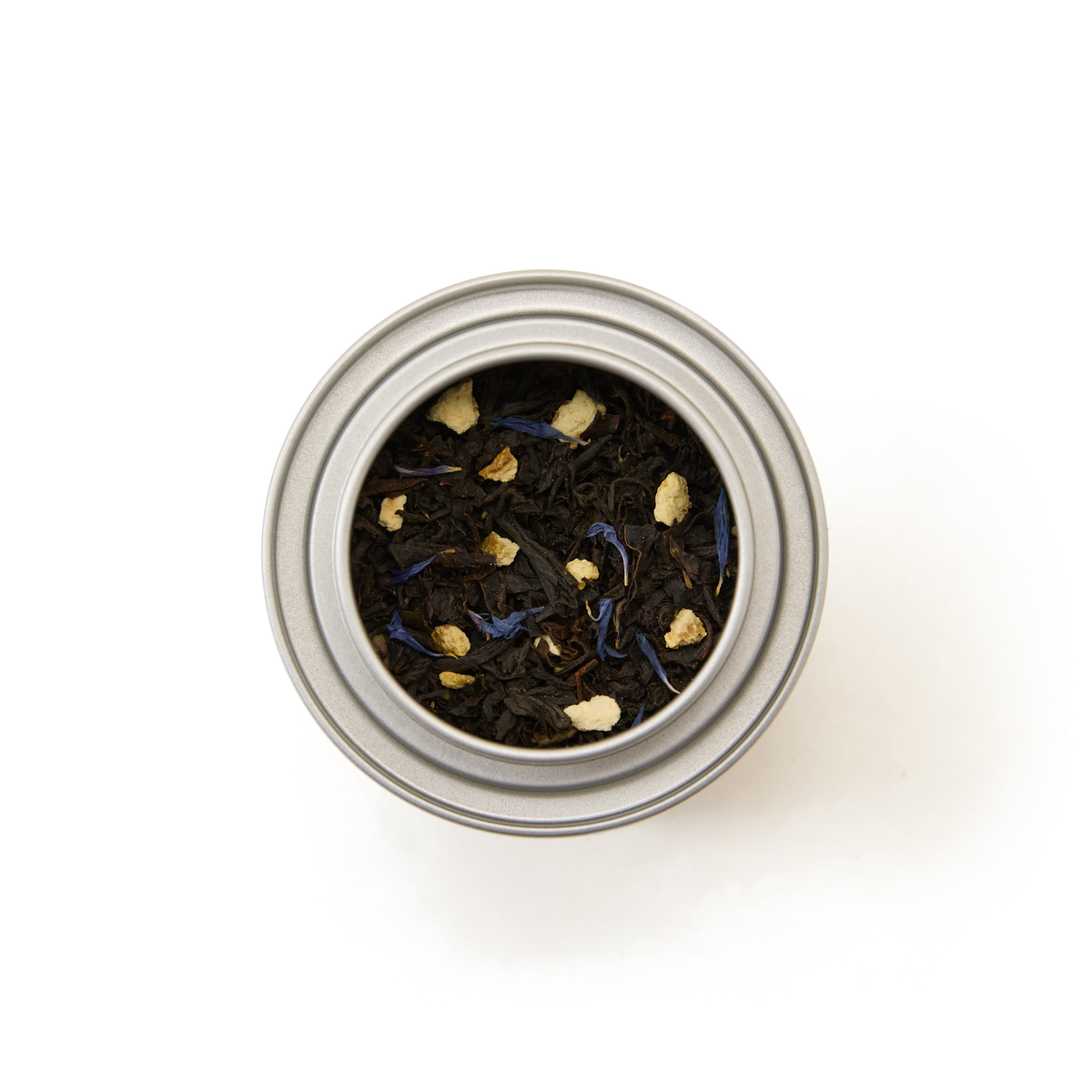 A top-down view of the Earl Grey Alice in Wonderland Mini Caddy, a metal tin filled with loose leaf black tea featuring dark leaves and visible pieces of dried fruit or spices, set against a white background—perfect for an elegant afternoon tea.