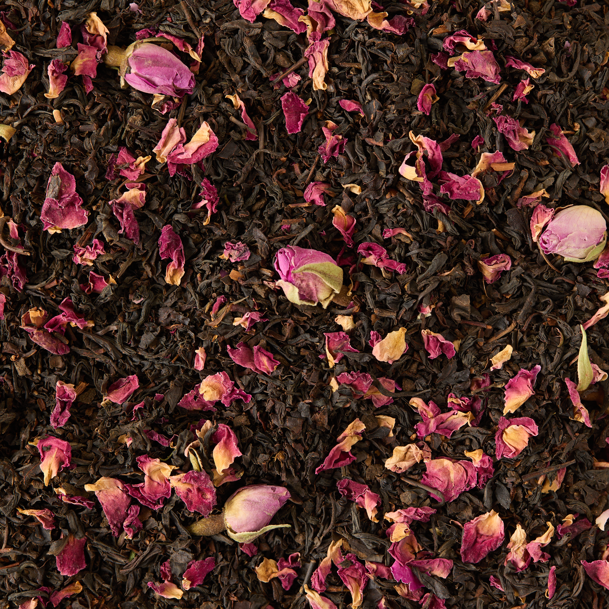 Loose black tea leaves blended with delicate dried rose petals and rosebuds are artfully scattered, forming a textured and vibrant background inspired by the English Rose Alice in Wonderland Mini Caddy—ideal for an elegant afternoon tea or anyone who appreciates a fragrant, floral black tea experience.