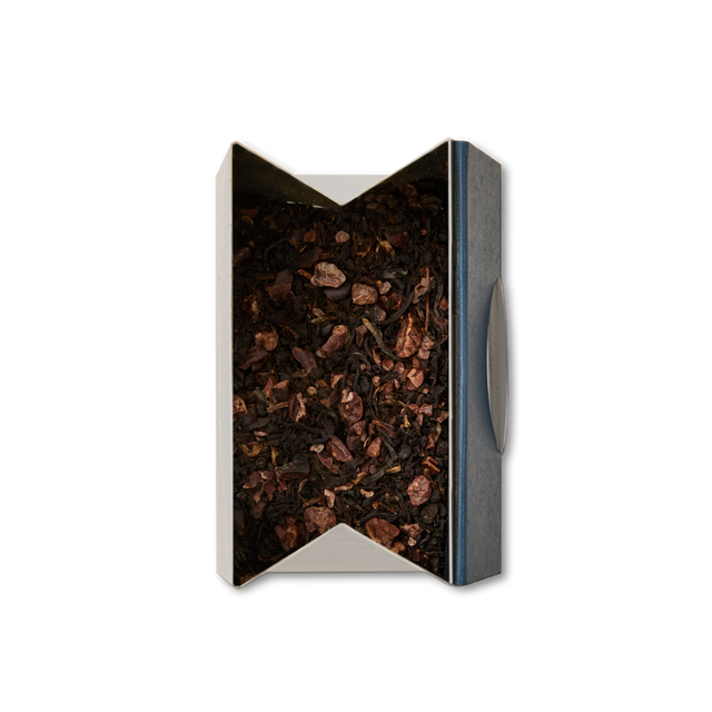 A top view of an open box of Dark Chocolate Loose Leaf Tea, featuring a blend of black tea mixed with small pieces of dried fruit and cocoa nibs, set against a white background.