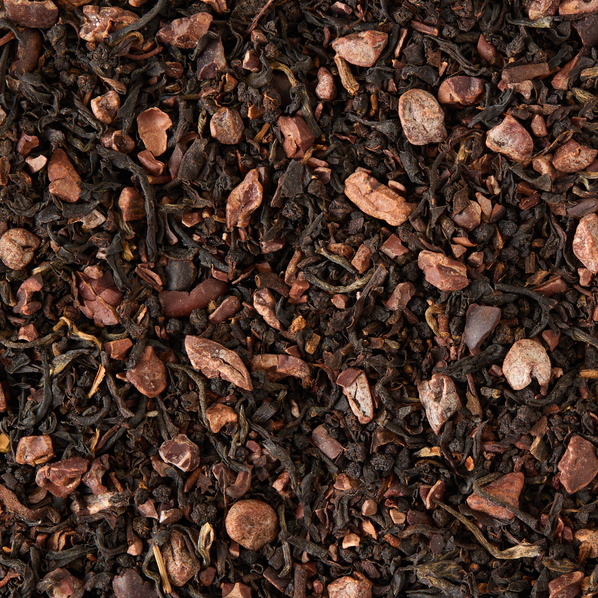 Dark Chocolate Loose Leaf Tea features a blend of black tea leaves and cocoa nib pieces, offering a mix of dark and light brown textures. The cocoa nibs are evenly distributed among the tea leaves, creating a rich, earthy look reminiscent of sugar-free chocolate.