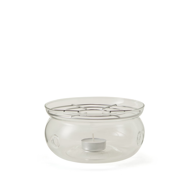 A clear glass fondue pot with a round base, open top, and metal grate above a small tealight candle holder at the bottom, used for heating or melting food items.