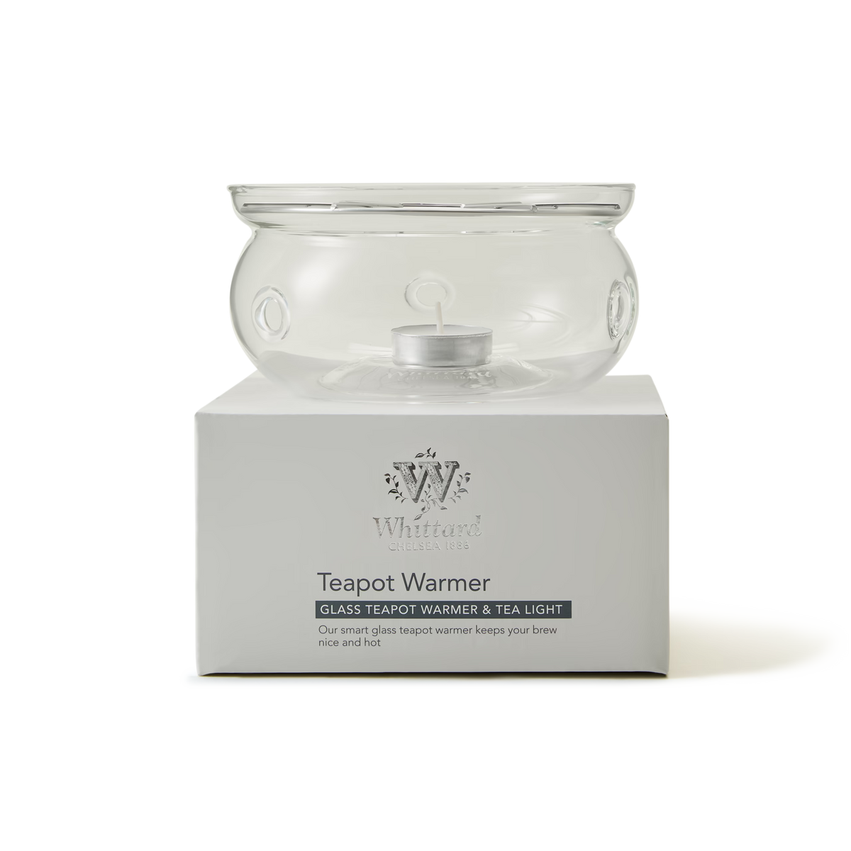 Clear glass teapot warmer with tea light inside, displayed on a white box labeled Teapot Warmer—Glass Teapot Warmer & Tea Light by Whittard of Chelsea.