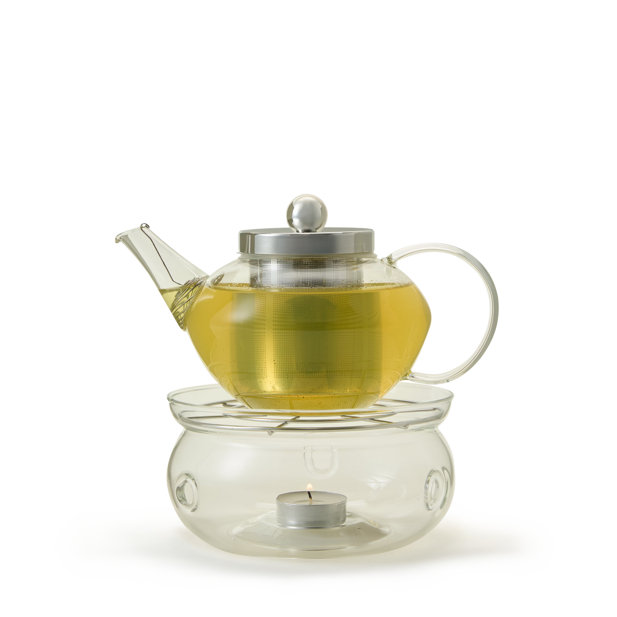 A glass teapot filled with yellow tea sits atop a glass warmer with a lit tealight candle inside, all placed against a white background.