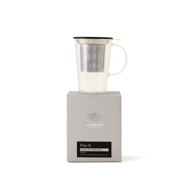 A clear glass mug with a metal infuser and black lid sits on top of a light gray box labeled Pao Glass Infuser Mug from Whittard of Chelsea. The background is plain white.