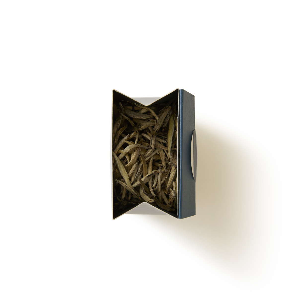A black box labeled “Silver Needle Loose Leaf Tea” is filled with long, thin dried tea leaves and sits on a white background, viewed from above—these delicate strands are characteristic of this rare tea, prized for its subtle flavor and exquisite quality.