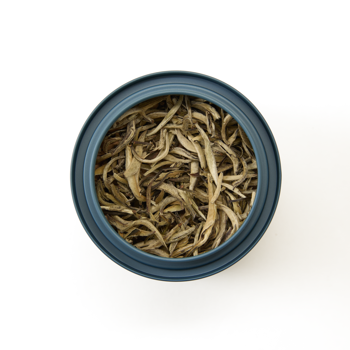 A top-down view of a blue container filled with long, thin, dried Silver Needle Loose Leaf Tea leaves arranged against a white background.