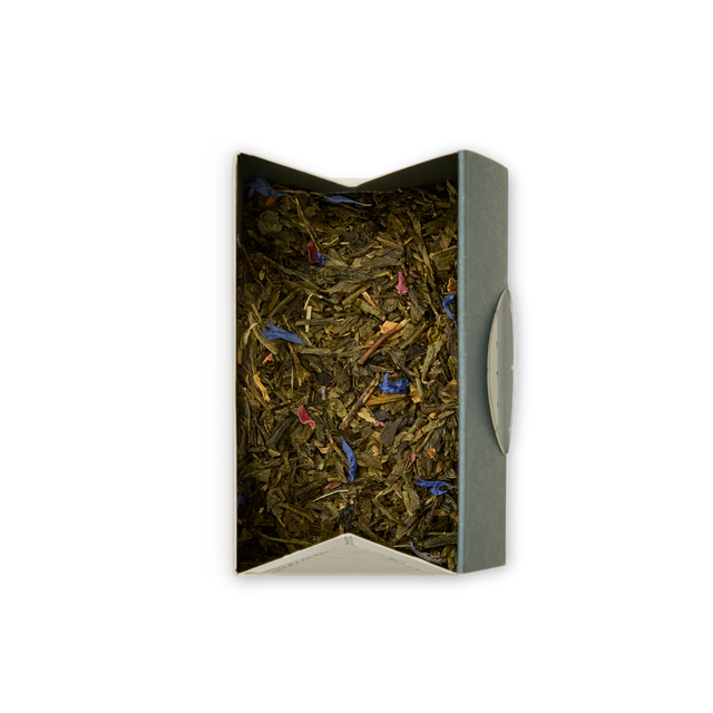 An open rectangular box of Mango & Bergamot Loose Leaf Tea, filled with vibrant green tea leaves blended with small blue and pink flower petals and a hint of mango bergamot, viewed from above against a plain white background.