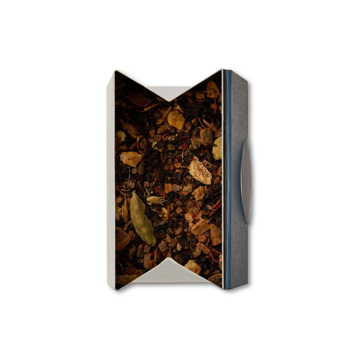 A top-down view of an open rectangular box containing Chilli Chai Loose Leaf Tea—a blend of dried tea leaves, spices, and herbs with visible cardamom pods and other ingredients—perfect for making a flavorful loose chai.
