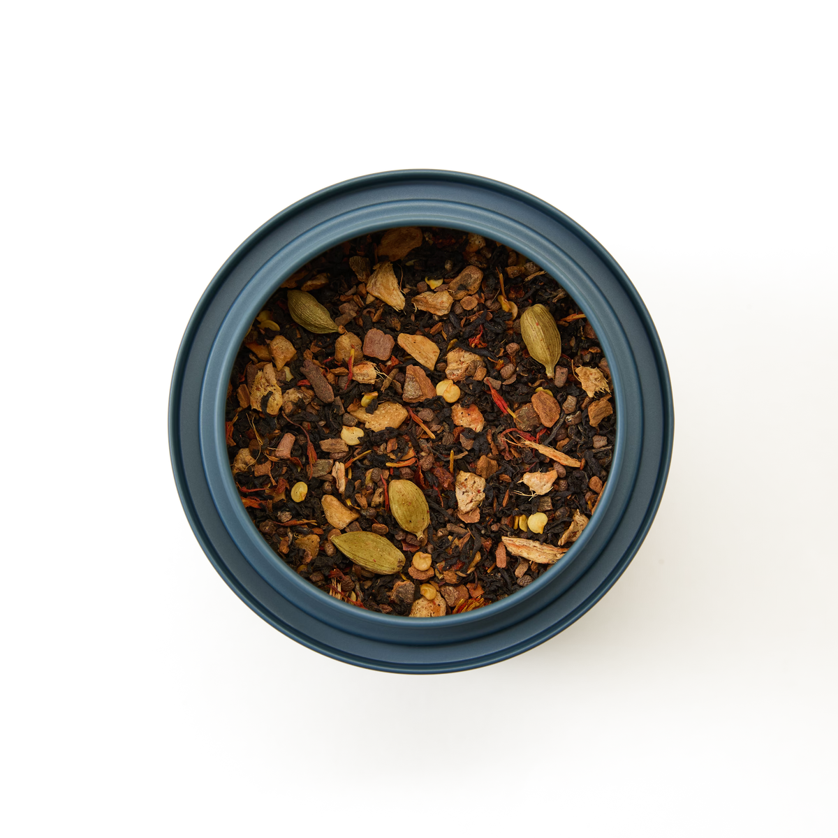 A round blue container of Chilli Chai Loose Leaf Tea, filled with a spicy blend of tea leaves, aromatic spices, and whole cardamom pods; viewed from above on a white background—perfect for brewing a bold chai or creamy chai latte.