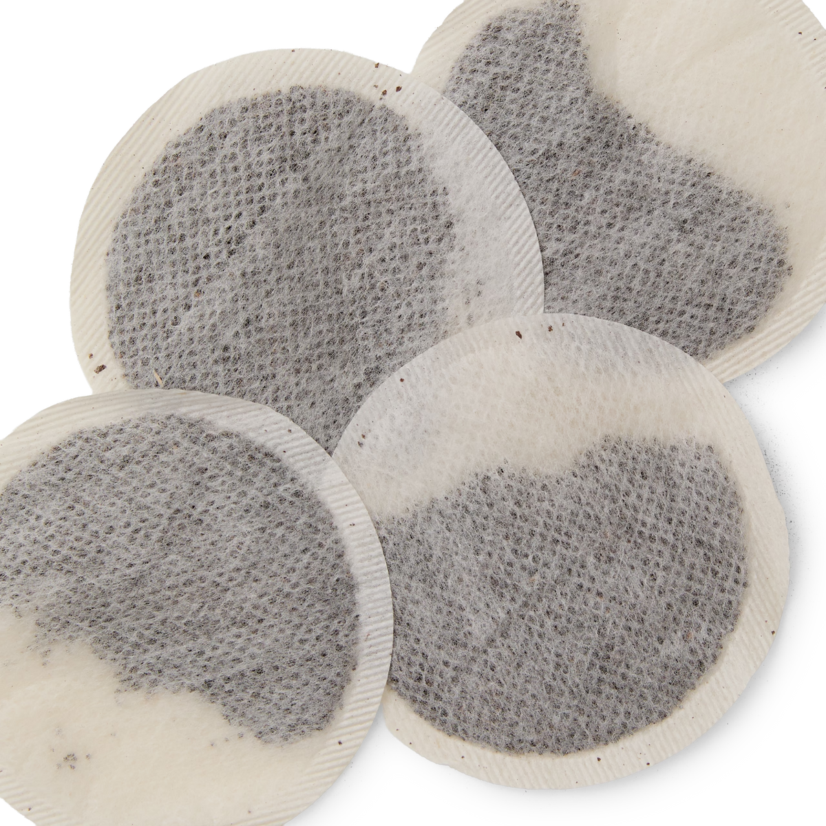 Four round, flat mesh English Breakfast teabags filled with loose Sri Lankan tea overlap each other against a white background.