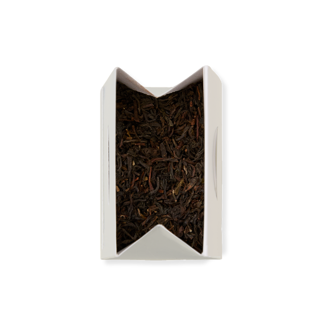 An open rectangular white box of Darjeeling Loose Leaf Tea, filled with loose black tea leaves and viewed from above on a plain white background.