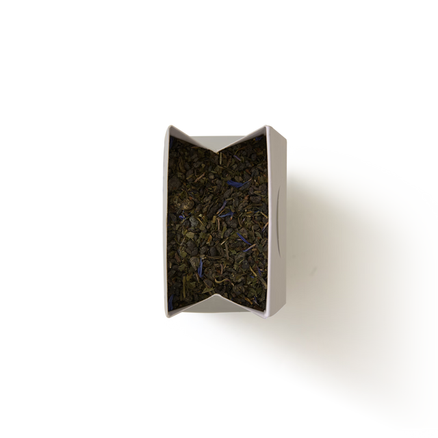 A top-down view of an open rectangular box filled with Marrakech Mint Loose Leaf Tea, displaying dark tea leaves and purple flower petals, set against a plain white background.