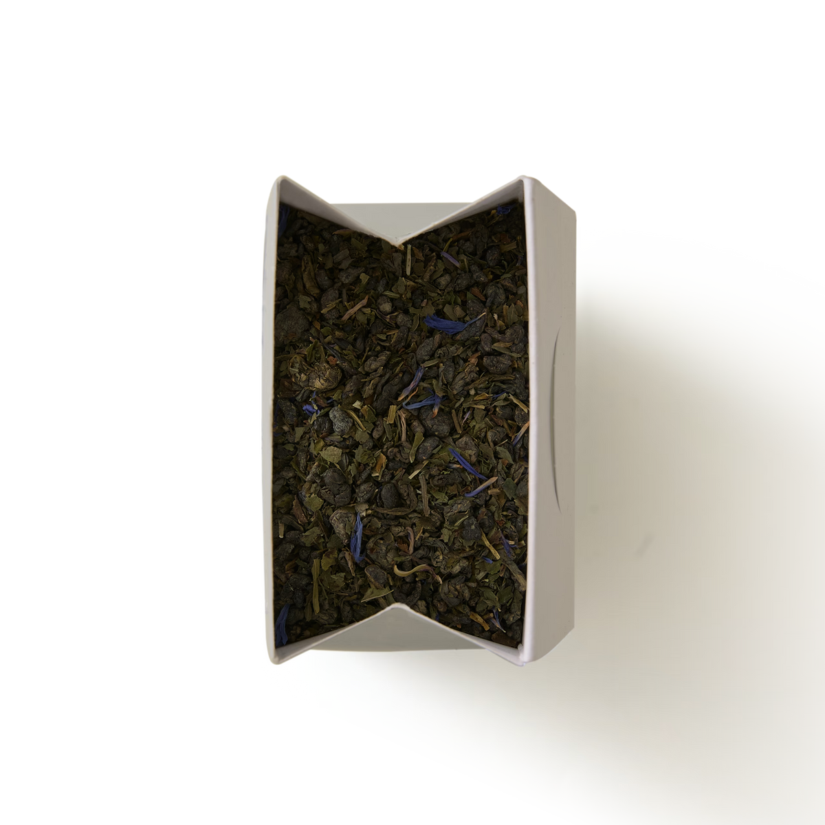 Top-down view of an open box of Marrakech Mint Loose Leaf Tea, showing loose green tea leaves, herbs, and small blue flower petals.