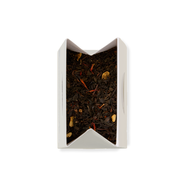 A partially opened white paper box of Spice Imperial Loose Leaf Tea reveals a blend of black tea leaves mixed with small pieces of dried ginger and red saffron threads, viewed from above on a white background.