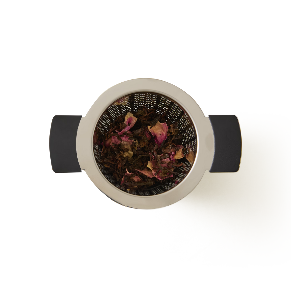 A top-down view of a metal tea infuser with black handles, containing loose leaf tea with visible dried rose petals, set against a white background.