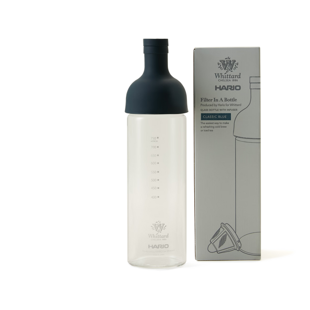 A clear glass Blue Hario Cold Brew Tea Bottle with a dark blue silicone top sits beside its box labeled “Whittard Hario Filter In A Bottle.” Both the bottle and the box display measurement markings up to 750ml and feature a Classic Blue label, making it perfect for preparing cold brew tea using authentic Japanese cold brewing techniques.
