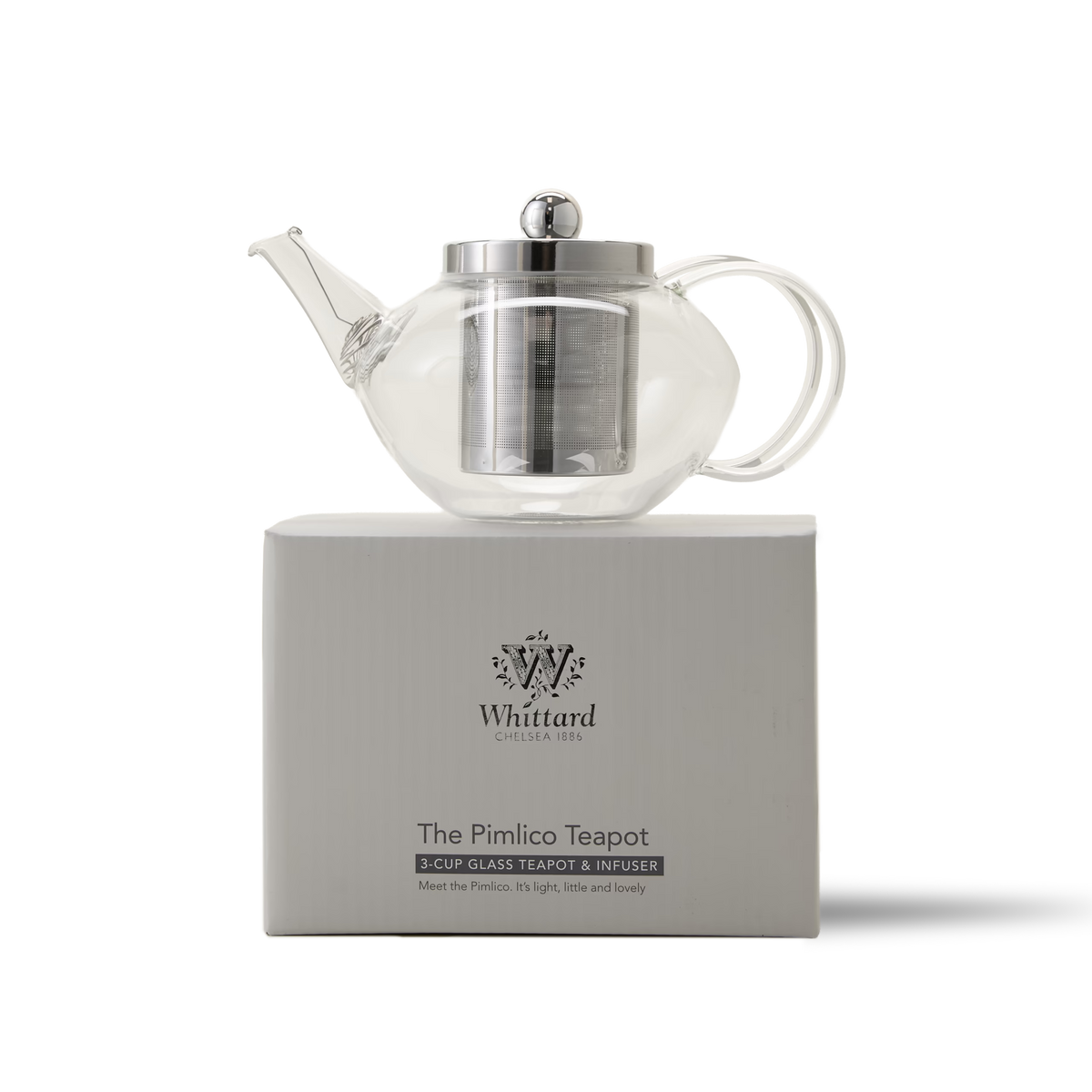 A clear glass teapot with a metal infuser and lid sits on a white Whittard box labeled The Pimlico Teapot. The box features the Whittard logo and brief product details.