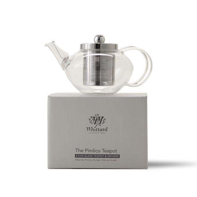 A clear glass teapot with a metal infuser and lid sits on a white Whittard box labeled The Pimlico Teapot. The box features the Whittard logo and brief product details.