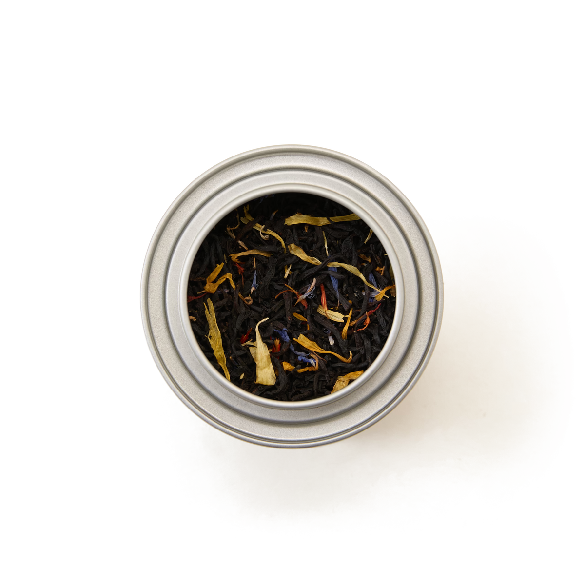 A top-down view of a silver tin filled with loose leaf black tea blended with colorful flower petals, set against a white background.