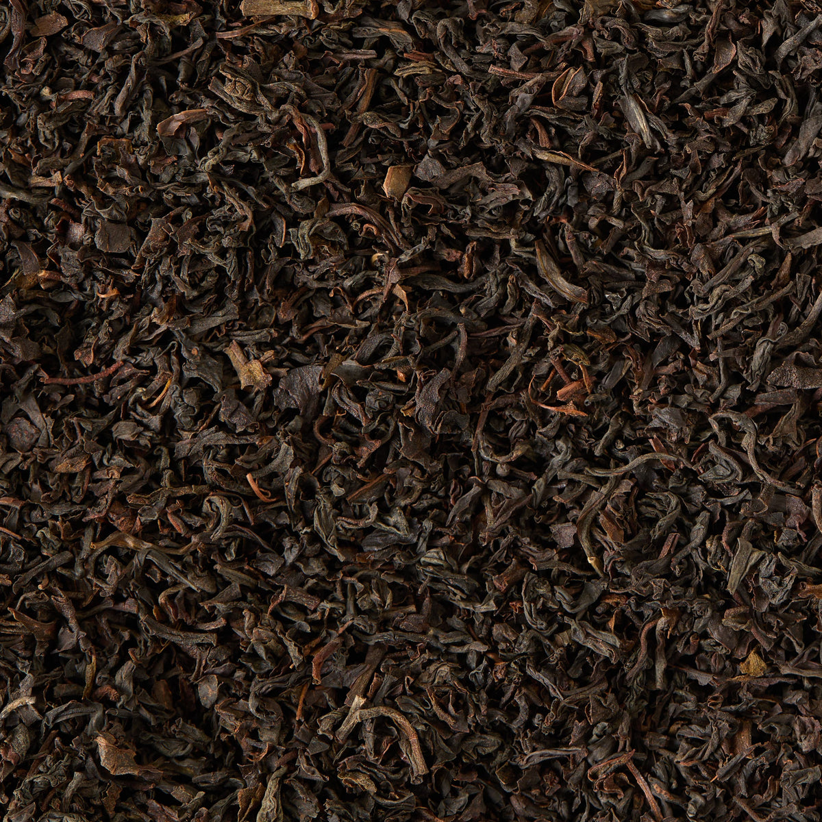 Loose black tea leaves, typical of the Chelsea Breakfast Loose Leaf Tea blend, are spread out to fill the entire image. The leaves display a dark brown, twisted appearance with subtle lighter brown and reddish hues throughout. Their dry and slightly crinkled texture reflects the premium quality characteristic of Chelsea Breakfast Loose Leaf Tea.