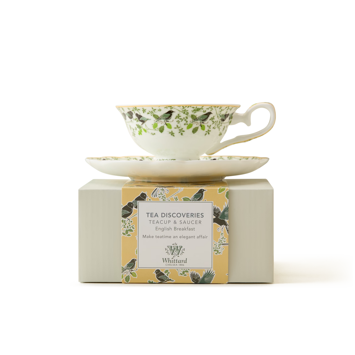 A floral-patterned teacup and saucer sit on a light box labeled Tea Discoveries Teacup & Saucer English Breakfast by Whittard, with a yellow border featuring birds and leaves.