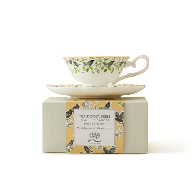 A floral-patterned teacup and saucer sit on a light box labeled Tea Discoveries Teacup & Saucer English Breakfast by Whittard, with a yellow border featuring birds and leaves.