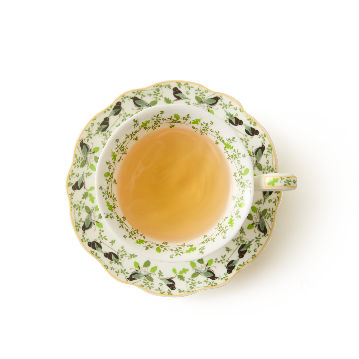 A cup of light tea in a decorative teacup with a green and black pattern, placed on a matching saucer, viewed from above against a white background.