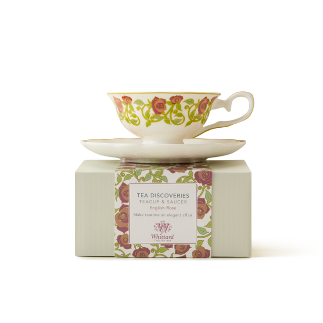 A floral teacup and saucer with a pink and green rose pattern sit atop a striped box labeled TEA DISCOVERIES ENGLISH ROSE by Whittard. The set is presented against a plain white background.