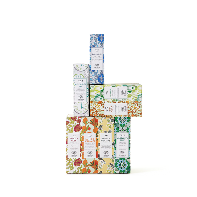A stack of colorful, patterned tea boxes forms a small tower. Each box features a different design and flavor label, displayed against a plain white background.