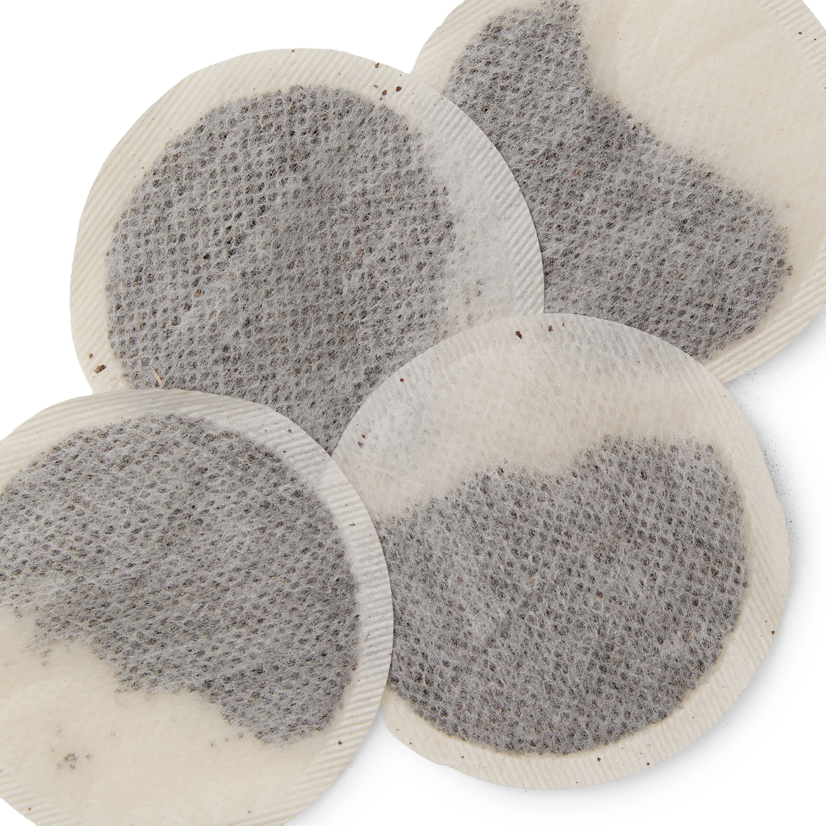 Four round, flat Earl Grey Teabags partially overlapping each other, filled with loose black tea leaves blended with fragrant bergamot, on a white background.
