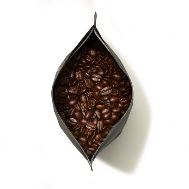 A top-down view of an open black bag filled with large Guatemala Elephant Coffee beans, showcasing their rich, roasted appearance against a white background.