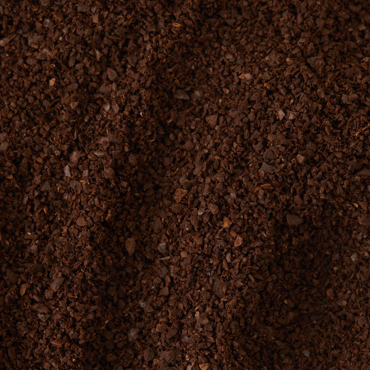 A close-up view of Café Français Coffee grounds, highlighting a coarse, dark brown texture with small, uneven granules densely packed together—perfectly capturing the rich character of this coffee.